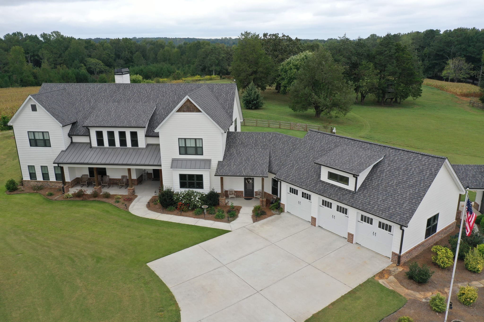 Aerial view of a large white house with a three-car garage and a wide driveway on a wooded property