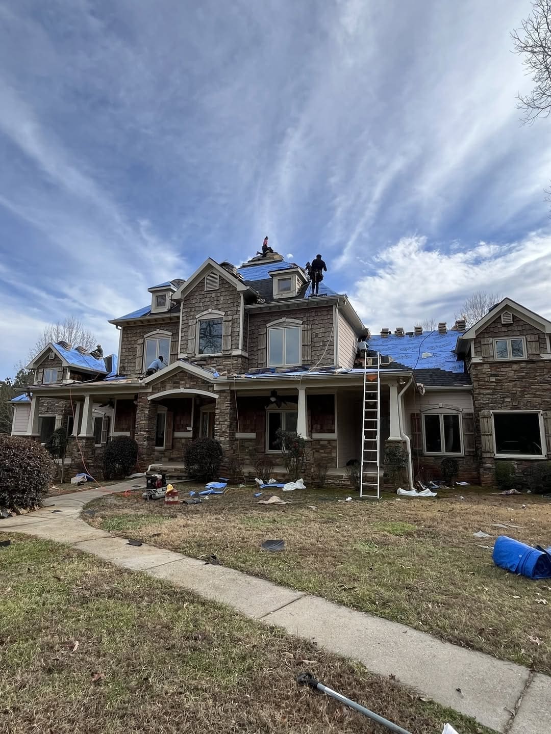 Roofers working on a large house with blue tarps covering the roof