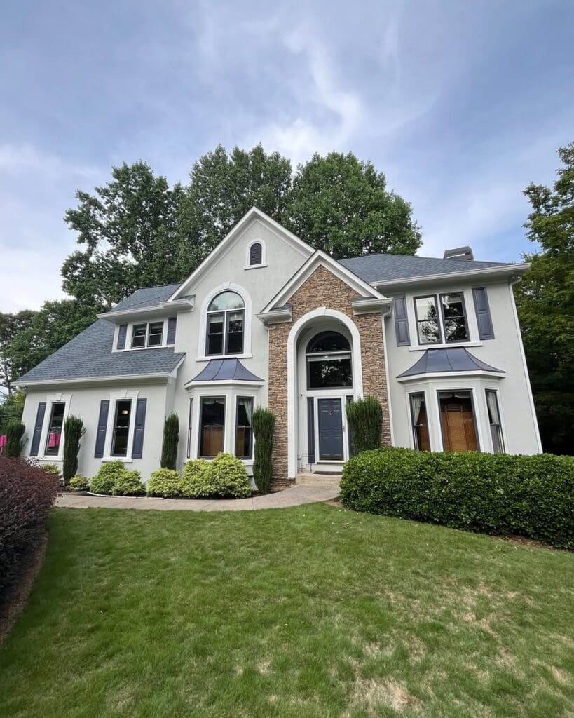 Two-story suburban house with a manicured lawn, trimmed hedges, and a stone-accented front entry