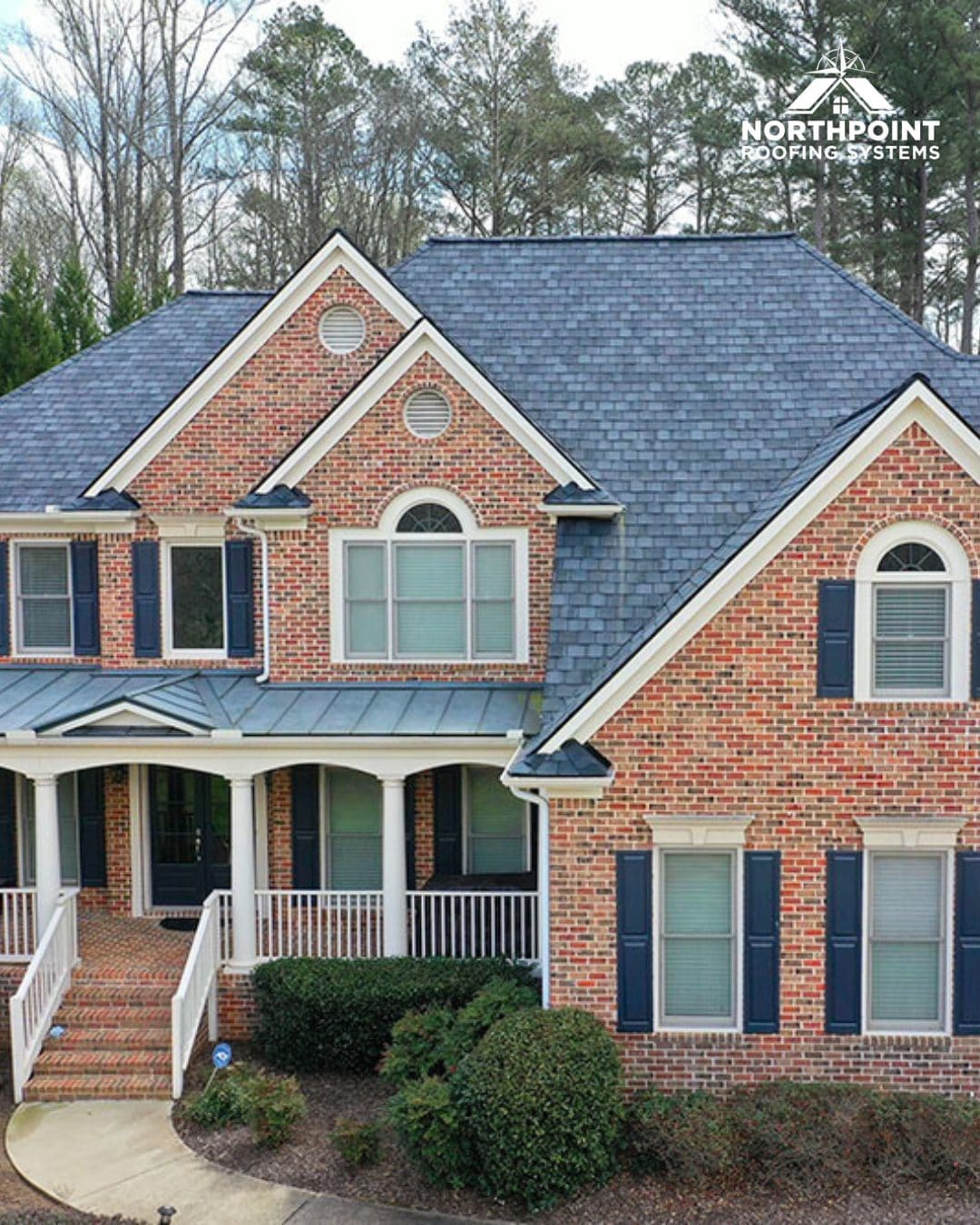 Brick house with a new blue-gray shingle roof and Northpoint Roofing Systems logo in the corner